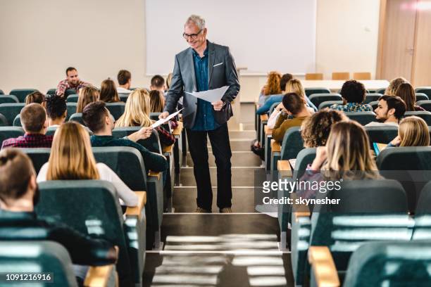 happy male professor giving his students test results in amphitheater. - amphitheater stock pictures, royalty-free photos & images