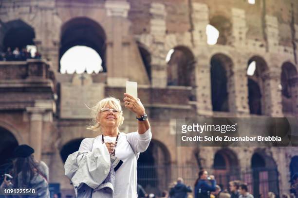blonde senior woman making a selfie in front of the roman coliseum - stadt personen rom herbst stock-fotos und bilder
