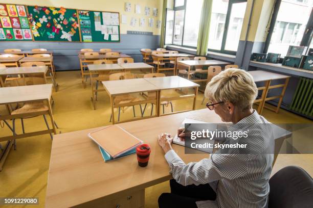 insegnante senior che prende appunti in classe vuota. - teacher desk foto e immagini stock