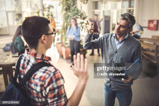 professore arrabbiato che comunica con uno studente di scuola superiore maschio in un corridoio. - white male professor foto e immagini stock