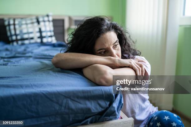 mujer preocupada sentado en el piso al lado de cama - mood fotografías e imágenes de stock