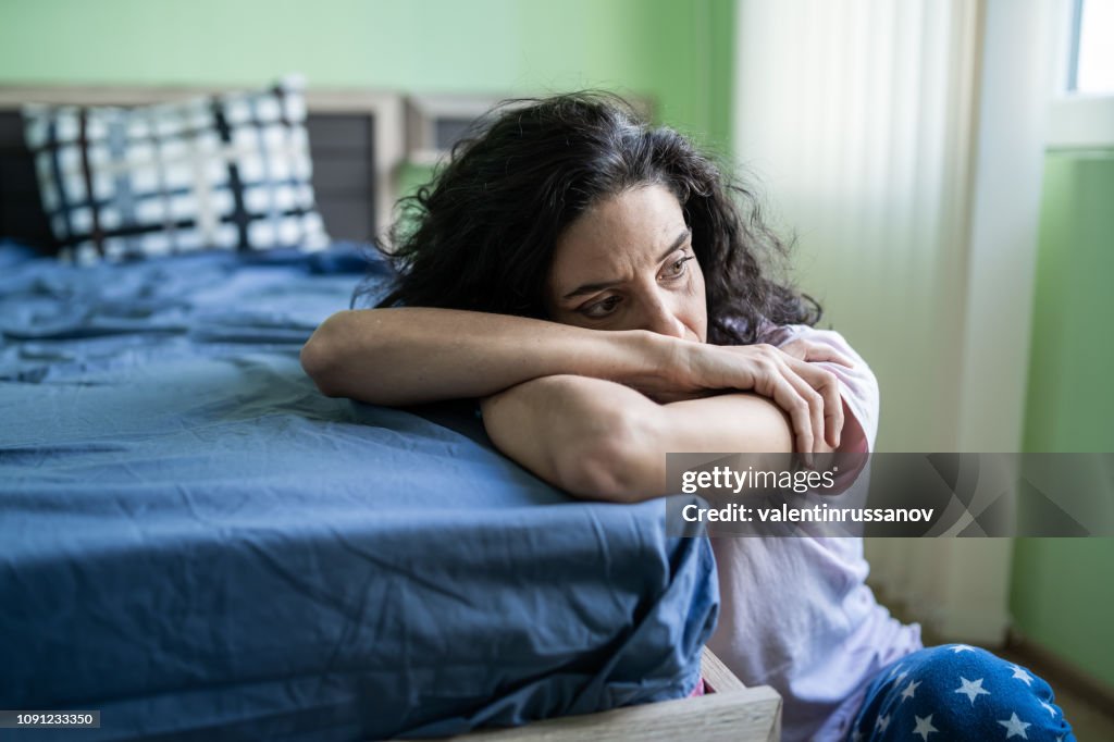 Worried woman sitting on floor next to bed