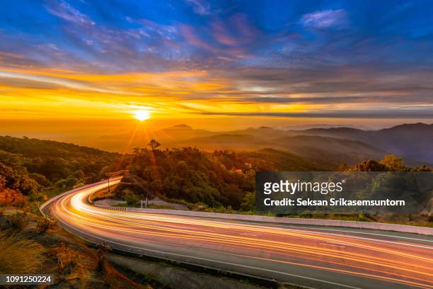 road light trails with sunrise in forest mountain - dirt road landscape sunset stock-fotos und bilder