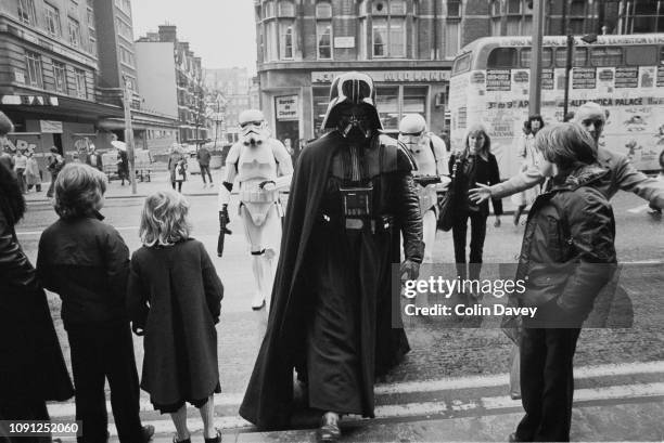 Man dressed in a Darth Vader costume followed by two other men dressed in Stormtrooper costumes cross a street in London as they are watched by some...