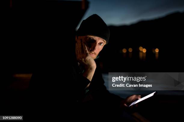 portrait of man using mobile phone while sitting at lakeshore against sky in olympic national park at dusk - dark sky stockfoto's en -beelden