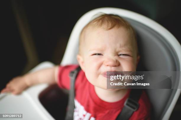 high angle portrait of cute baby girl sticking out tongue while sitting on high chair at home - human tongue foto e immagini stock