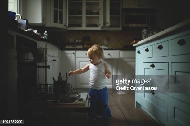 cute baby girl holding kitchen utensils while standing in kitchen at home - dark clothes stock pictures, royalty-free photos & images