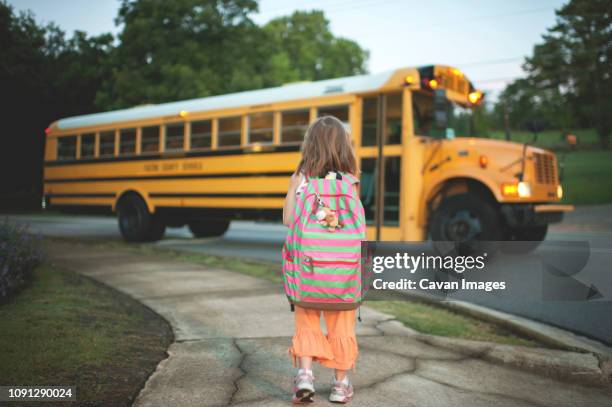 rear view of schoolgirl with backpack waiting for bus while standing on footpath - school bus stock photos et images de collection