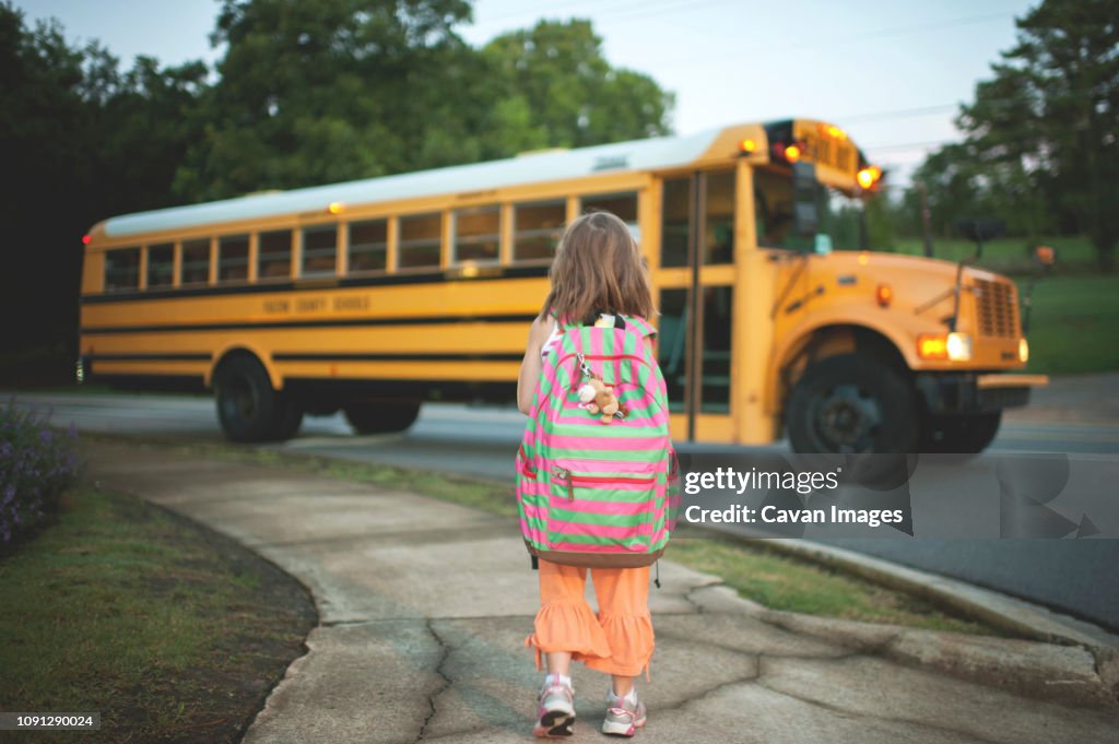 Rear view of schoolgirl with backpack waiting for bus while standing on footpath