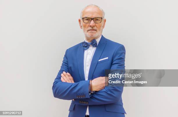 portrait of confident senior man in suit with arms crossed standing against white background - 蝶ネクタイ ストックフォトと画像