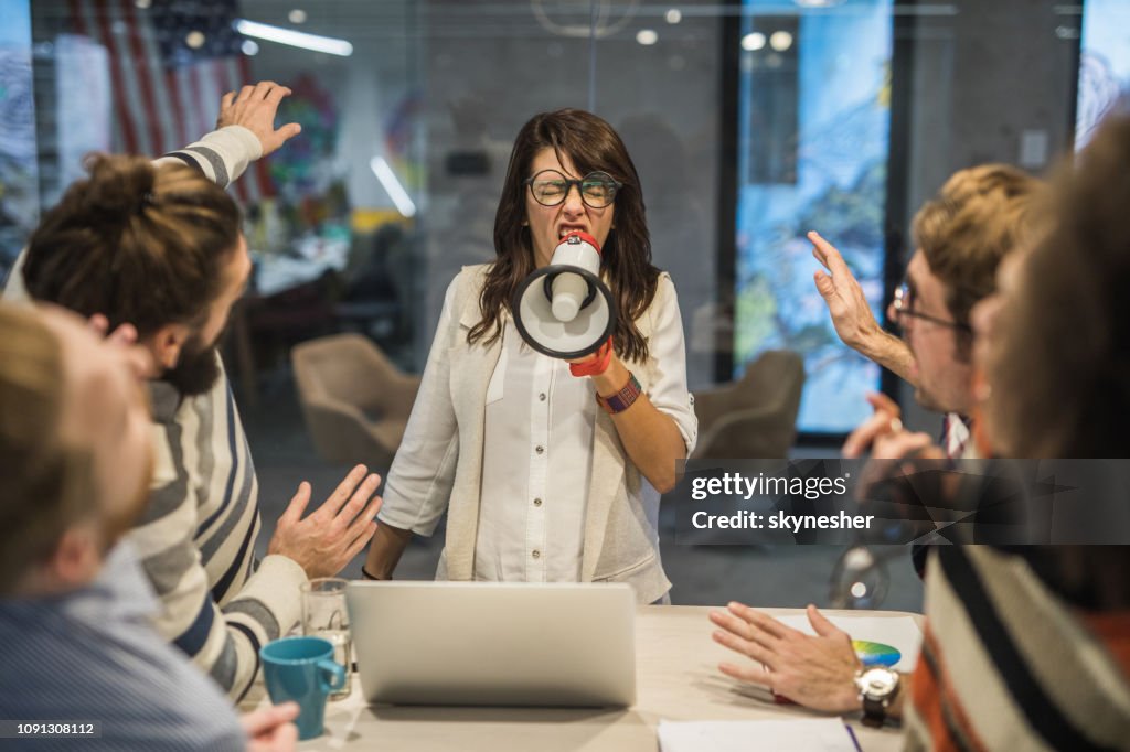 Rude female leader yelling at her coworkers through megaphone in the office.