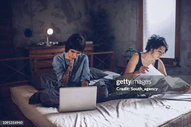 lesbian couple paying bills in bed - worry free stock pictures, royalty-free photos & images