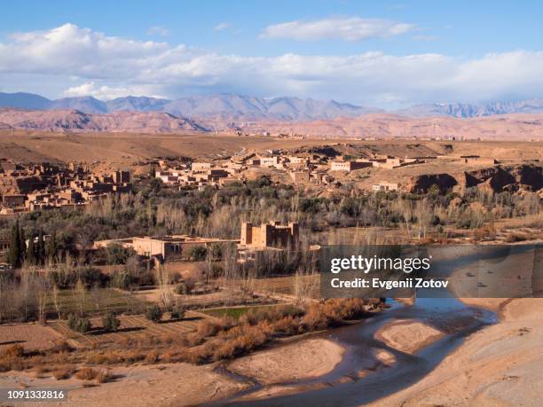 village with small ksar on the riverbank in the dades valley with the high atlas mountains on the background. morocco - maroc atlas photos et images de collection