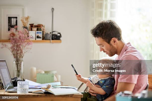 man met laptop en papieren kijken speelse zoon - financieel item stockfoto's en -beelden