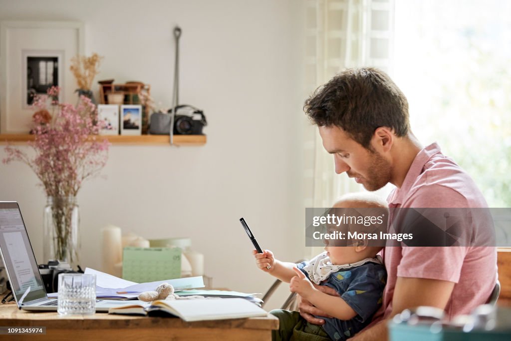 Man with laptop and papers looking at playful son