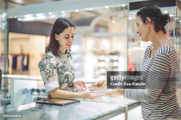 young woman is buying a necklace at the shopping mall - jeweller stock pictures, royalty-free photos & images