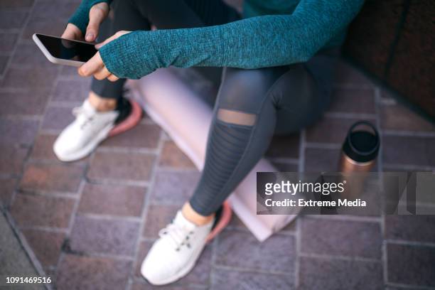 actieve sporten vrouw met behulp van haar mobiele telefoon zittend in een stad straat - mobile apps stockfoto's en -beelden