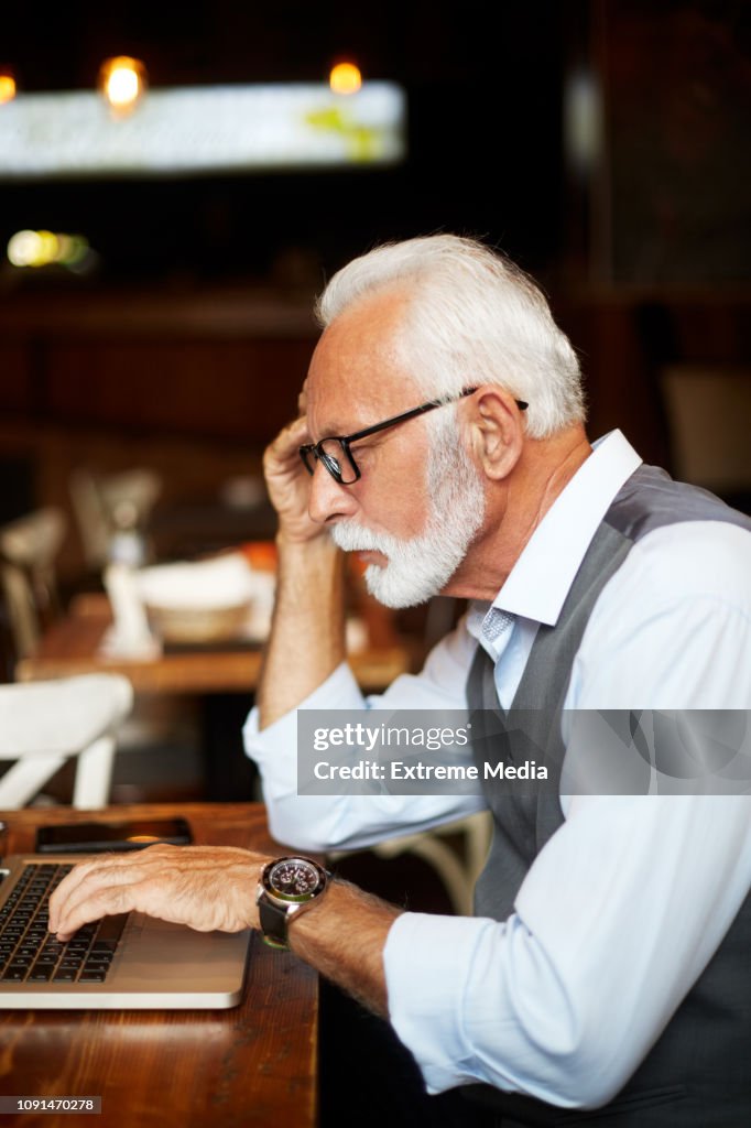 Elderly manager concentrates hard while working on a laptop in a cafeteria