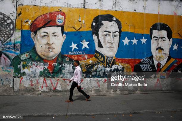 Man walks past a mural depicting Venezuela's late President Hugo Chávez, Latin American independence hero Simon Bolivar and Venezuela's President...