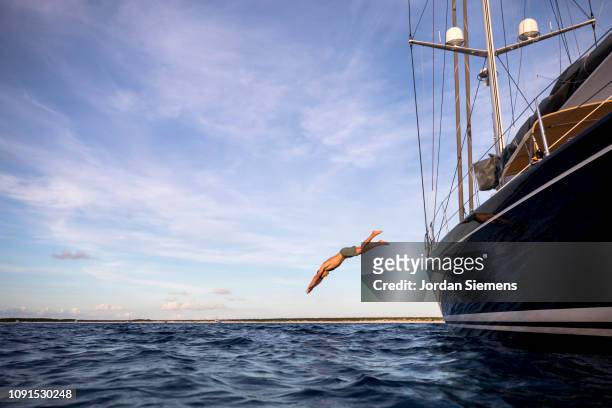 a man diving off the side of a sailboat. - jumping of boat foto e immagini stock