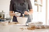 Woman in apron adding cocoa powder to the batter in bowl.
