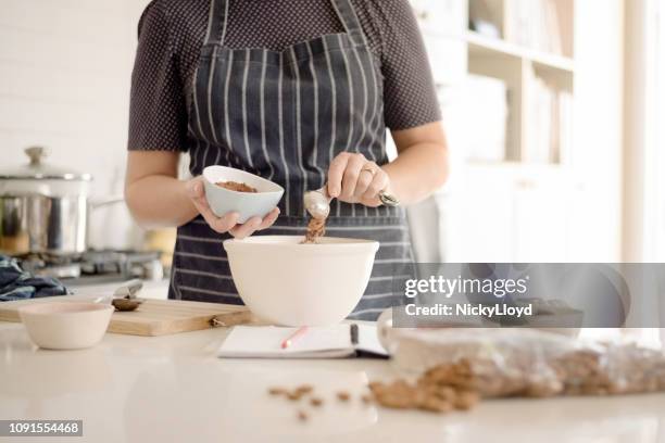 woman in apron adding cocoa powder to the batter in bowl. - misturar imagens e fotografias de stock