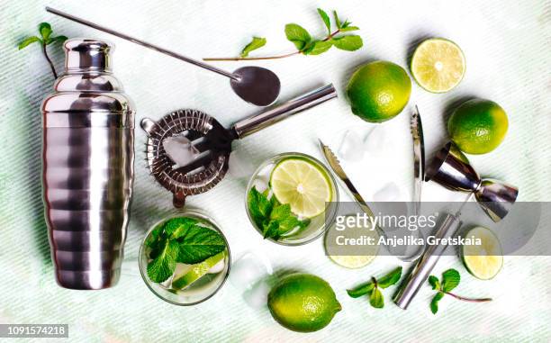 summer drink mojito ingredients - white rum, lime, mint, and ice, and set of bar tools for making a cocktails arranged on a stone background. - mojito stock-fotos und bilder
