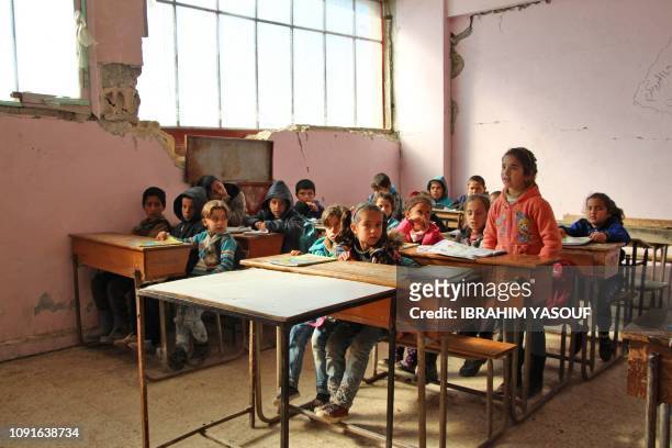 Syrian children attend class in a damaged classroom at a school which was hit by bombardment in the district of Jisr al-Shughur, in the west of the...