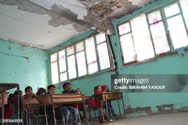 Syrian children attend class in a damaged classroom at a school which was hit by bombardment in the district of Jisr al-Shughur, in the west of the...