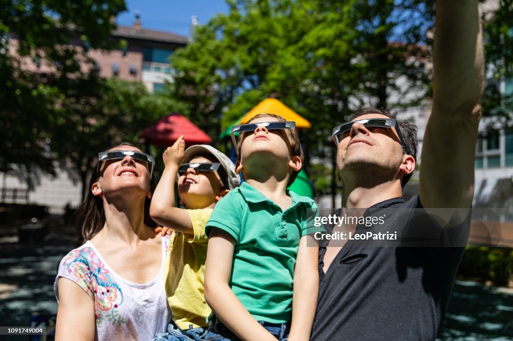 All the family look at solar eclipse in the city street in a public park