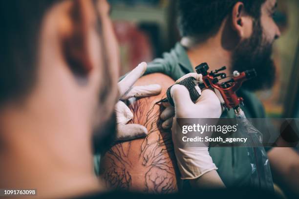 artist tattooing a man in studio - tribal arm tattoo stock pictures, royalty-free photos & images