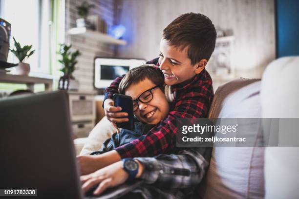 two teenage boys with gadgets on couch at home - bros stock pictures, royalty-free photos & images