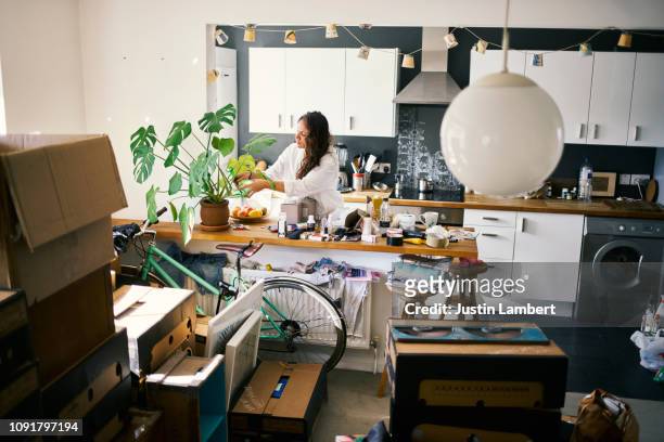 woman watering her plants in the process of moving house - messy kitchen stock-fotos und bilder