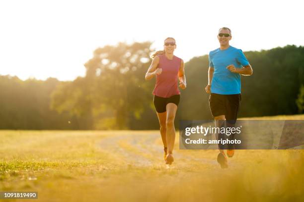 twee passen sportieve uithoudingsvermogen lopers samen joggen op zonnige zomerdag in grasland - 40s couple sunny stockfoto's en -beelden