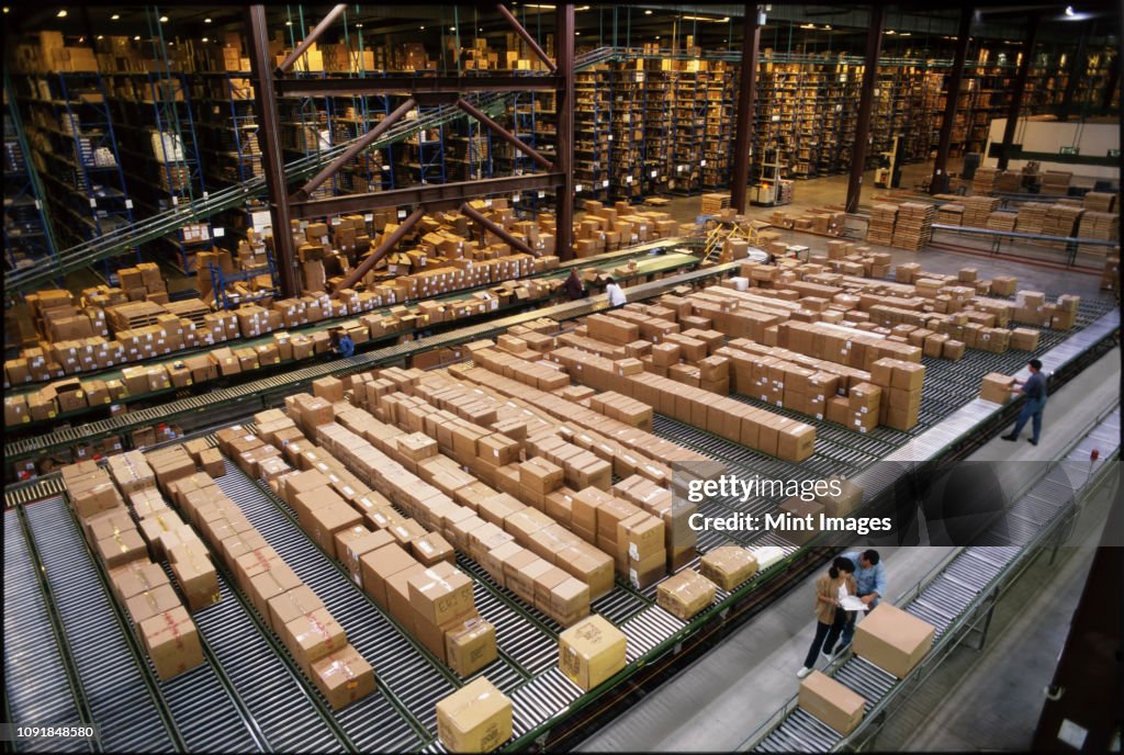 Overview of a large industrial distribution warehouse storing products in cardboard boxes on conveyor belts and racks.
