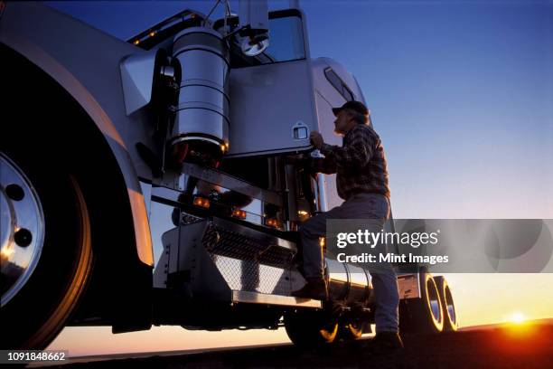 a silhouette of a truck driver getting into the cab of his commercial class 8 truck tractor at sunrise. - trucker fotografías e imágenes de stock