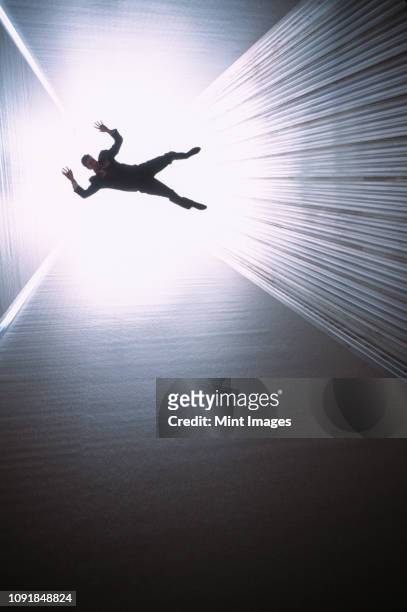a conceptual silhouette of a businessman appearing to be falling down a long shaft lit by a bright light at the end. - man silhouette back lit stock pictures, royalty-free photos & images