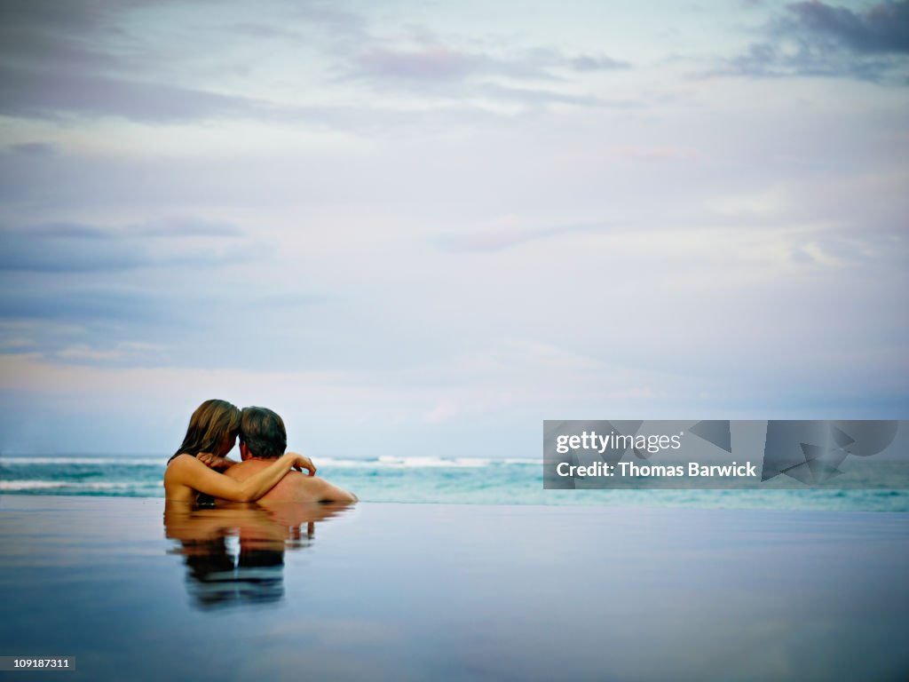 Couple embracing in infinity pool rear view