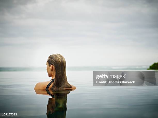 woman standing in infinity pool overlooking ocean - rustige scène stockfoto's en -beelden