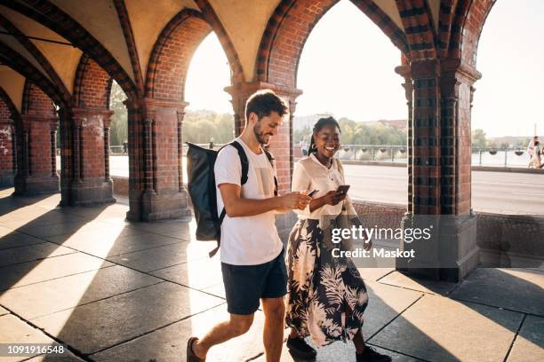 young male and female friends walking on footpath in city - berlin people ストックフォトと画像