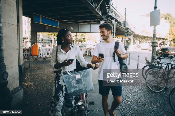 smiling multi-ethnic friends talking while walking on sidewalk in city - leben in der stadt stock-fotos und bilder