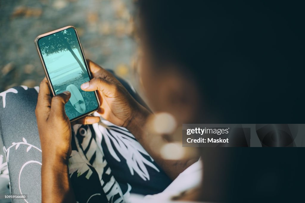 High angle view of young woman looking at beach photograph on smart phone