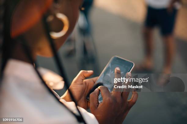 cropped image of young woman using smart phone while standing on street in city - rear view photos stockfoto's en -beelden