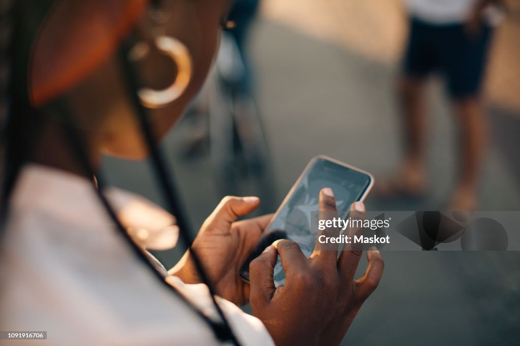 Cropped image of young woman using smart phone while standing on street in city