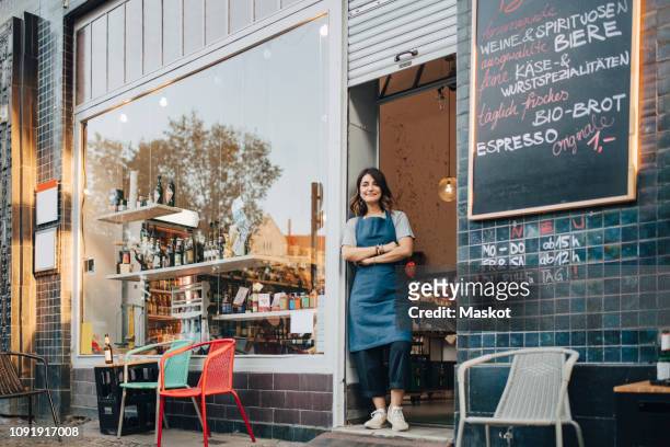 full length portrait of female owner standing at entrance of deli - berlin cafe stock pictures, royalty-free photos & images