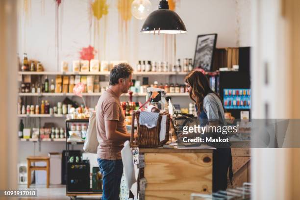 side view of female sales clerk with customer at checkout counter in deli - deli counter stockfoto's en -beelden