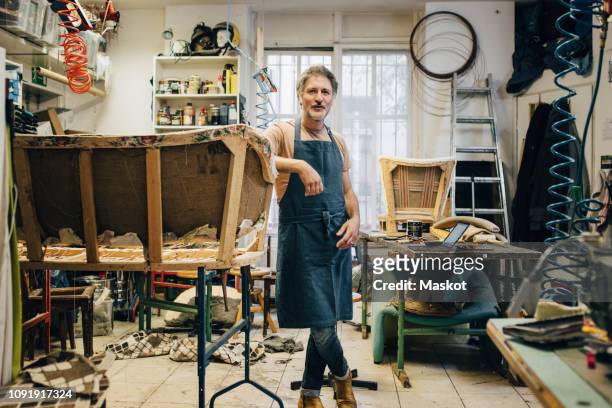 Portrait of mature male craftsperson standing by incomplete sofa in upholstery workshop