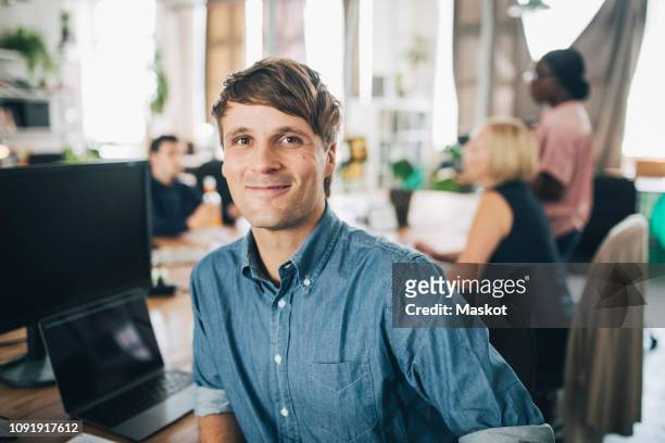 portrait of confident businessman sitting at desk in creative office - solo un uomo di età media foto e immagini stock