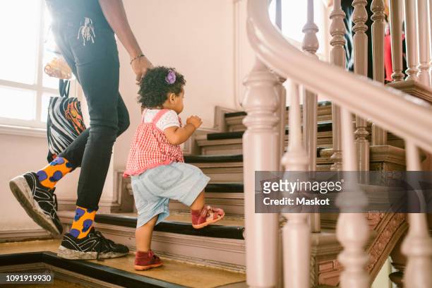 baby girl holding hand of father while climbing staircase at apartment - family tree stockfoto's en -beelden