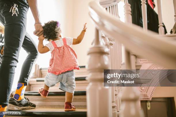 baby girl holding hand of father while climbing steps in apartment - family tree stockfoto's en -beelden